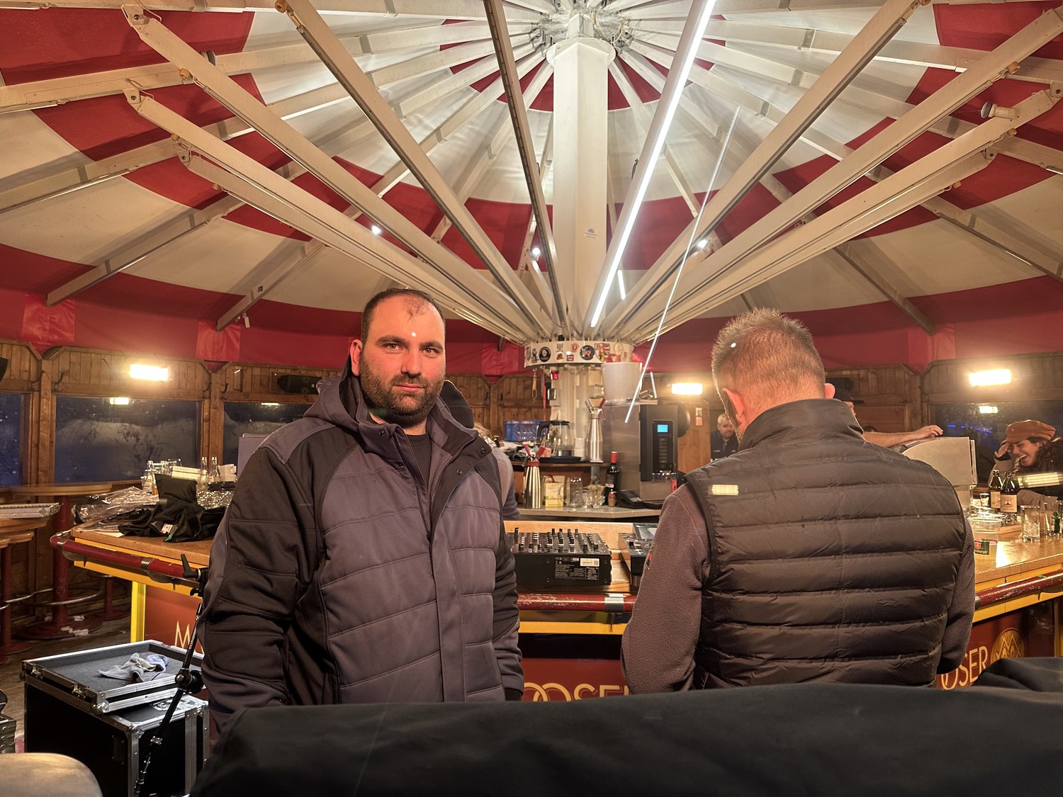 Blick in ein Festzelt mit rot-weißer Zeltdecke, Bar und aufgebautem Mischpult