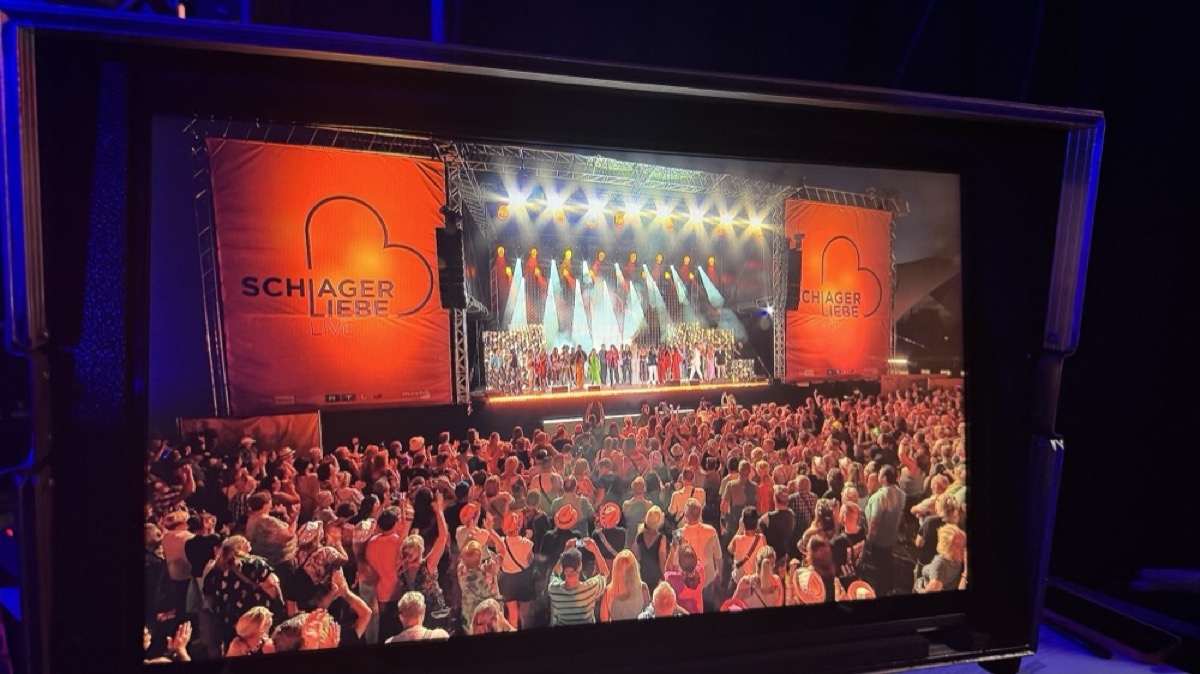 Große LED-Wand über einer Bühne mit Chor, davor ein voll besetzter Saal in warmem Licht