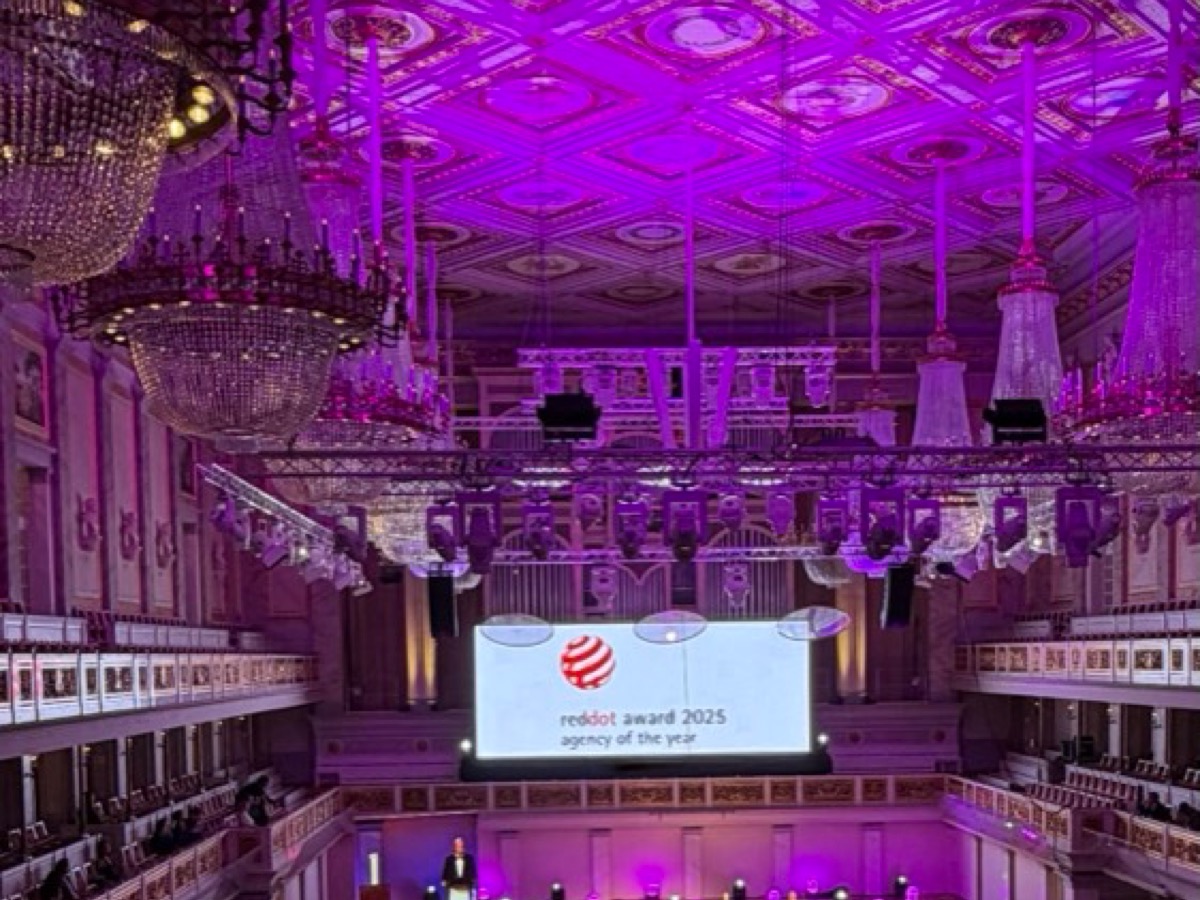 Historischer Konzertsaal mit Kassettendecke und Kronleuchtern in magentafarbenem Licht, darunter eine Traverse mit Scheinwerfern und eine Leinwand