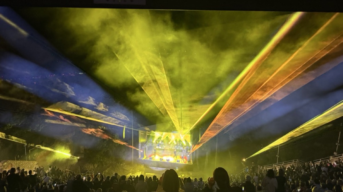Konzertbühne mit gelben Lichtstrahlen über dem Publikum in einer abgedunkelten Halle