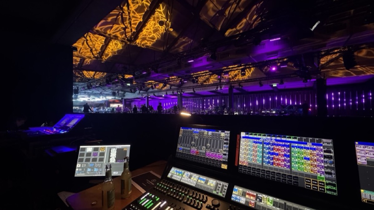 Lichtpult und Monitore am Regieplatz, im Hintergrund die beleuchtete Veranstaltungshalle