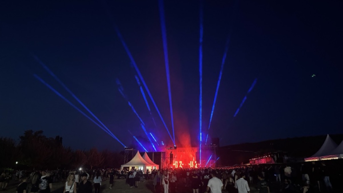 Blaue Lichtstrahlen über einem Veranstaltungszelt bei Nacht, davor Besucher auf dem Freigelände